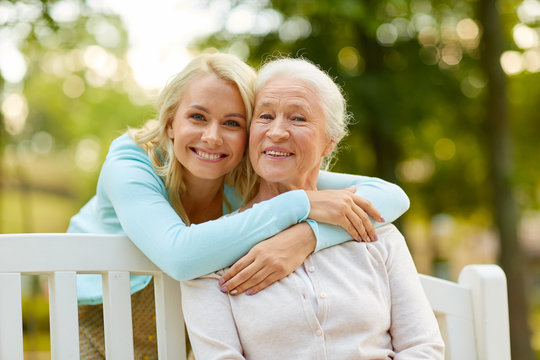family, generation and people concept - happy smiling young daughter with senior mother sitting on park bench and hugging