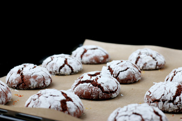 Chocolate cookies with cracks on baking paper and iolated on black. Cracked chocolate biscuits