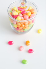 food, confectionery and sweets concept - close up of glass jar with colorful candy drops over white background