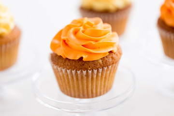 food, pastry and sweets concept - cupcake with orange buttercream frosting on glass confectionery stand over white background