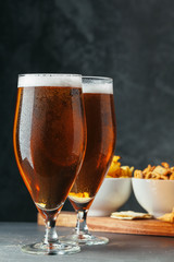 Glass of lager beer with snack bowls on dark stone background