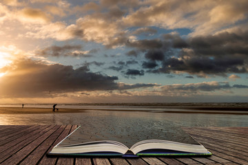Obraz na płótnie Canvas Stunning Winter sunrise over West Wittering beach in Sussex England with wind blowing sand across the beach in pages of open book, story telling concept