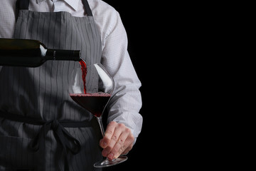 the waiter pours wine in glass on dark background - obrazy, fototapety, plakaty