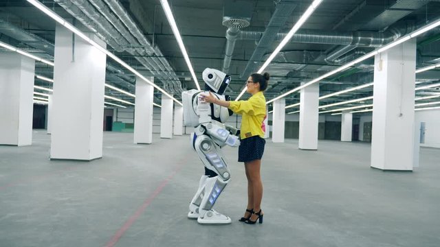 Tall robot is coming to a girl and embracing her