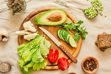 Fototapeta na wymiar Ingredients for green salad with a piece of bread. Make a fresh salad of avocado, greens, peas, parsley, cabbage, cucumber and apples.Vegetables on a wooden board. Top view.