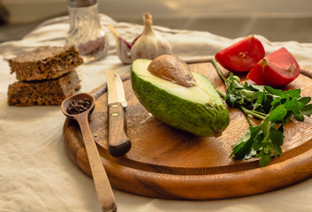 Ingredients for guacamole on a wooden board. Parsley, avocado, tomatoes, garlic, black pepper.
