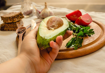 Ingredients for guacamole on a wooden board. Avocado in a hand of young woman.