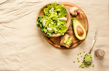 Fresh delicious green salad with avocado in a wooden plate and gluten free toast. Top view. Healthy lunch dish and Diet detox food concept.