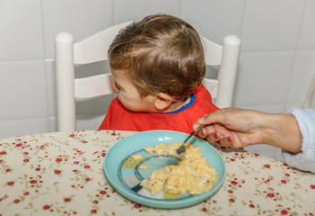 A boy with a bib refuses to eat food at the kitchen table in his house