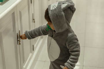 A cute little boy with a pajamas and a pacifier, is playing in the hallway of his house.