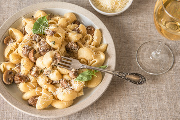 Homemade pasta carbonara with mushroom cream sauce on a plate close-up and a glass of dry white wine - Italian cuisine, lunch.