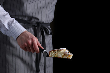 chef holding a piece of cake on black background. pie making and serve