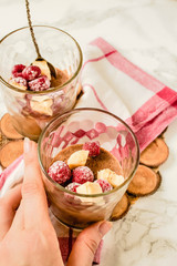 Chocolate mousse (soufflé) from aquafaba. Vegan dessert in jars on a white marble background. In the hands of a young woman.Close-up.
