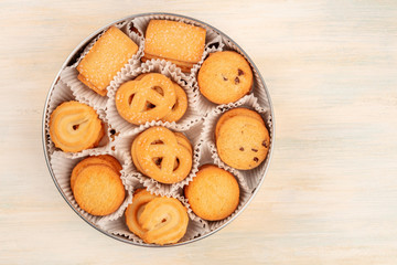 A photo of Danish butter cookies in the traditional tin box, shot from the top on a white wooden background with copy space