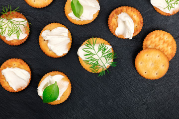 A photo of salt crackers with soft cream cheese spread and herbs, shot from the top on a black background with a place for text