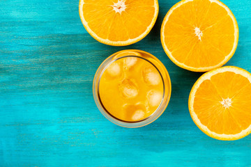A glass of fresh orange juice with orange halves, shot from the top on a vibrant blue background with copy space