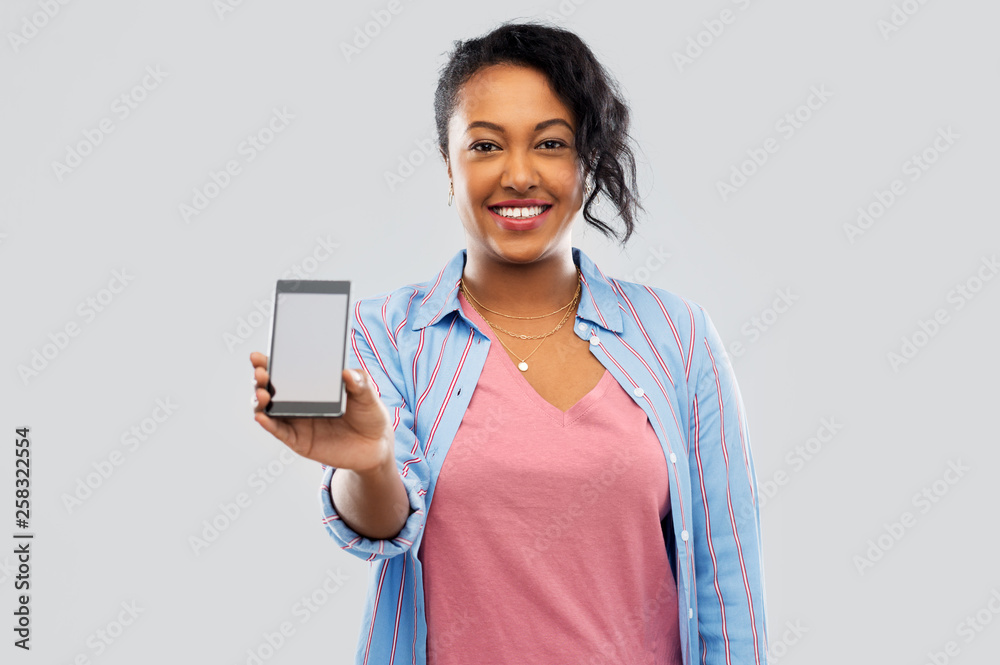 Sticker technology and people concept - happy african american woman showing blank screen of smartphone over grey background