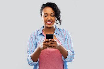 technology and people concept - happy african american woman using smartphone over grey background