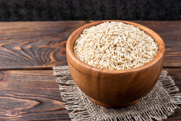 Brown rice on dark wooden background.