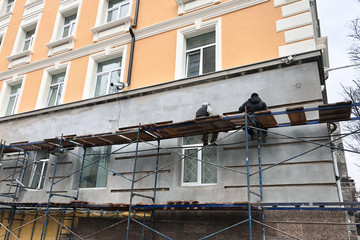 two workers sit on scaffolding and paint the wall of the house. scaffolding near the wall of the house, reconstruction of old city buildings exterior.