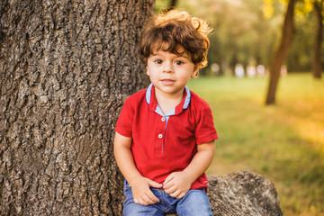 Portrait of very handsome sunshine little toddler boy playing at summer city park. Calm child with...