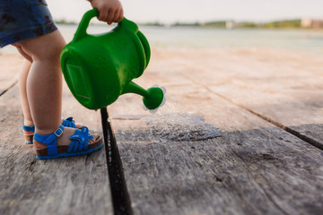 A small girl is playing with a watering can of a wooden bridge. Spring and summer. Gardening. green watering can