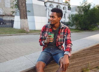 Break time! Young african man with coffee cup sitting on city street