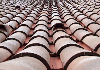 full frame diminishing perspective view of an old roof with curved clay red tiles in lines with ventilation slots