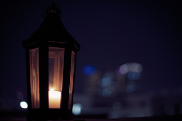 Ornamental Arabic lantern with burning candle glowing at night and glittering golden bokeh lights. Dark background. city lights at the background