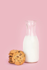 Cookies y botella de leche sobre fondo rosa vista de frente. Copy space
