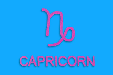 Symbol of astrological sign and word capricorn cut out of purple paper on blue table. Top view. Horoscope concept