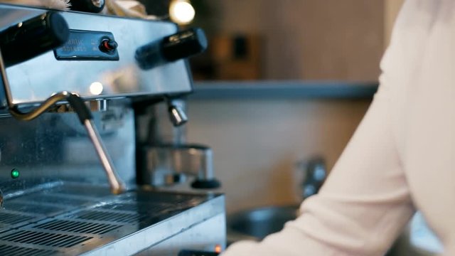 The girl fills a cup with hot water from the coffee machine. Hands close up. Hand girl baristas dub coffee from holder coffee machines