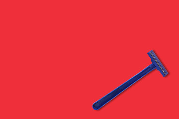 One male disposable plastic razor blue color with two sharp blades on red table in bathroom with copy space for your text. Top view. Hygiene concept