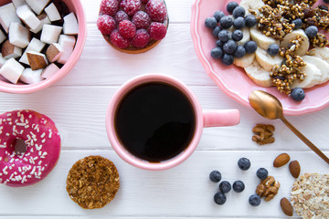Trendy served table with healthy food, tasty pink doughnut and low fat cookies. Banana and coconut pieces, granola and little merengue. Pink color plates and cup. 