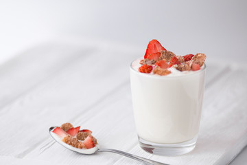 Natural yogurt  with strawberry and multigrain flakes on a white wooden table. Front view
