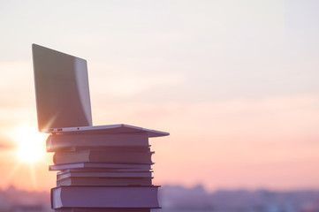 Laptop and a lot of books on the sunset town background. Education concept