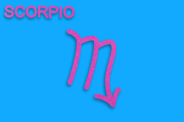 Symbol of astrological sign and word scorpio cut out of purple paper on blue table. Top view. Horoscope concept