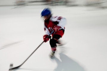 Young hockey player in red dress with blue helmet in movement.