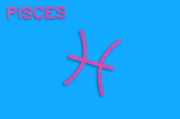 Symbol of astrological sign and word pisces cut out of purple paper on blue table. Top view. Horoscope concept
