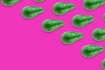 Diagonal rows of green whole fresh raw avocados on pink background with copy space for your text