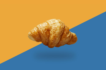 Croissant flying in air on yellow and blue background. Food levitation minimalism.