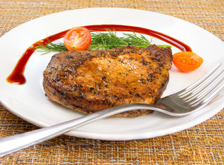 Steak meat with tomato and lettuce salad leaf and fork in a white plate