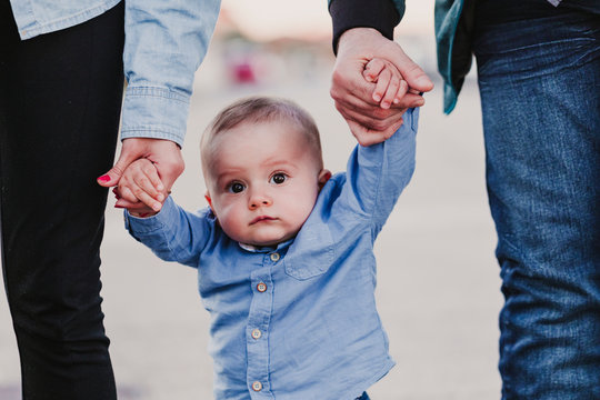 Happy Stylish Parents Holding Hands With Baby Boy And Walking By The Street, Tender Family Moment.