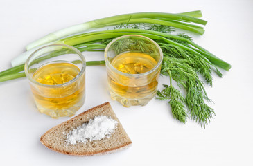 Pepper vodka in two transparent glasses, green onions, dill, rye bread and coarse salt - still life.