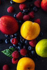Creative flatlay with fresh fruits and berries on dark background. Grapes, blueberries, raspberries with peaches and lime