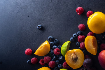 Creative flatlay with fresh fruits and berries on dark background with copy space. Grapes, blueberries, raspberries with peaches and lime