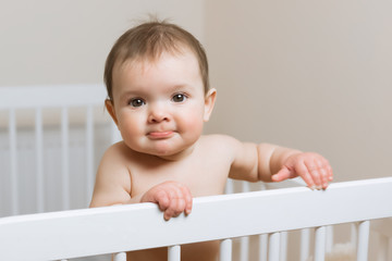 Baby girl in a diaper playing in the crib. Very funny face expression.