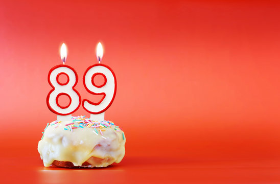 Eighty nine years birthday. Cupcake with white burning candle in the form of number 89. Vivid red background with copy space