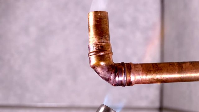 Flame from a gas blowtorch being applied to a copper pipe fitting, to melt solder and seal the joint.