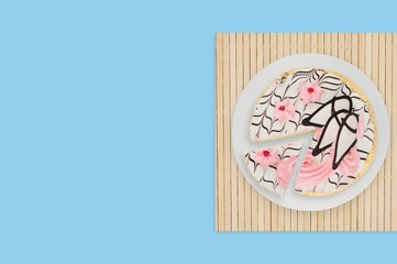 One cuted decorated creamy cake in white circle plate on bamboo mat on blue table. Top view. Celebration concept. Copy space for your text